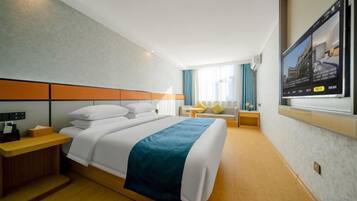 Habitación de hotel con cama, mesita de noche, lámpara y televisor montado en la pared.