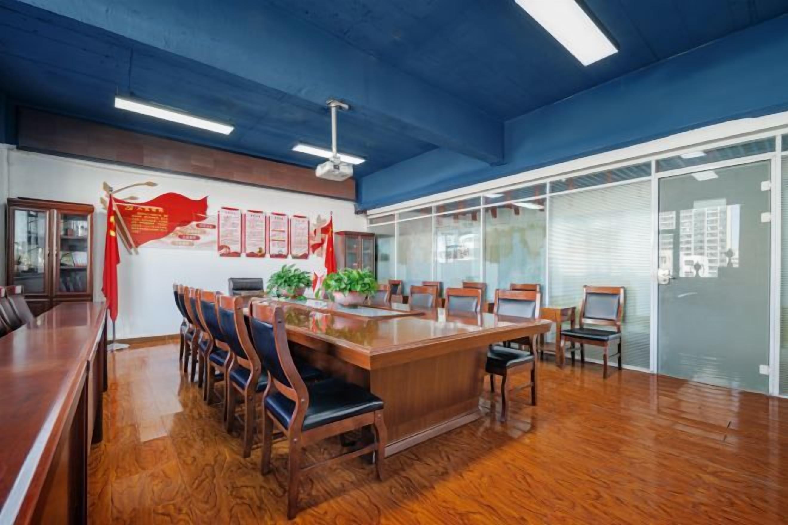 Une salle de conférence avec une longue table, des chaises, un ventilateur de plafond et une cloison vitrée avec des fenêtres.