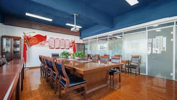 Una sala conferenze con un lungo tavolo, sedie, una ventola a soffitto e una parete divisoria in vetro con finestre.