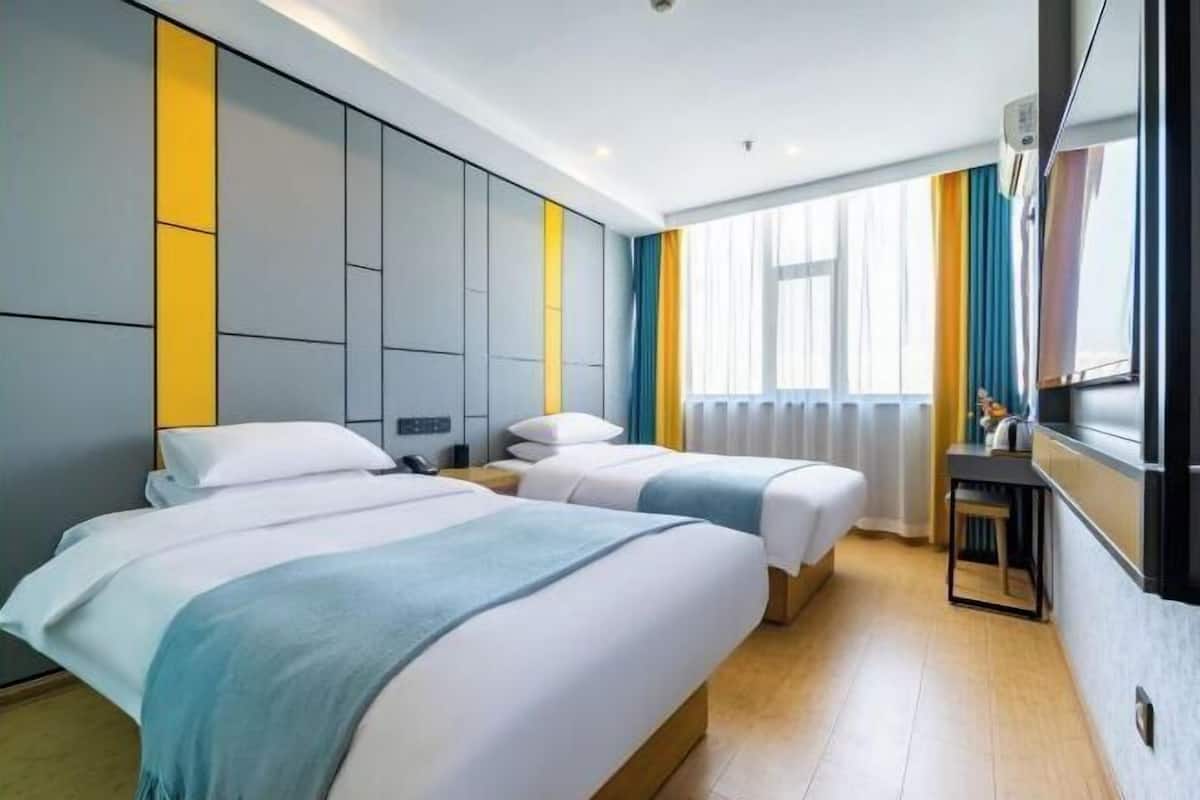 Une chambre d’hôtel avec deux lits, un petit bureau et une grande fenêtre avec des rideaux.