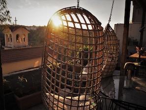 A hanging chair with a bamboo frame, a glass table, and a view of a building with a cross. - Yhouse (Athens)