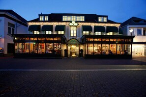 A building with a prominent 'Riche' sign, multiple storefronts, and a brick-paved entrance.
