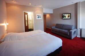 A hotel room with a bed, a grey sofa, a TV, and a red carpet.