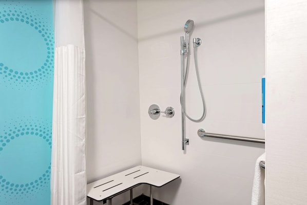 Un espacio de ducha con cabezal de ducha de mano, grifo de pared y un perchero para toallas.