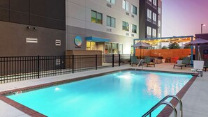 Ein Hotelpoolbereich mit einem klaren, blauen Pool, einem Zaun und Sitzgelegenheiten im Freien mit Sonnenschirmen.