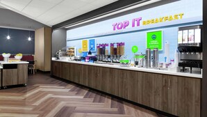 Un área de desayuno con un mostrador que exhibe diversas opciones de comida y un letrero que dice "TOP IT BREAKFAST".