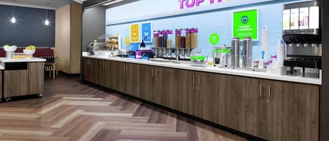 Un área de desayuno con un mostrador que exhibe diversas opciones de comida y un letrero que dice "TOP IT BREAKFAST".