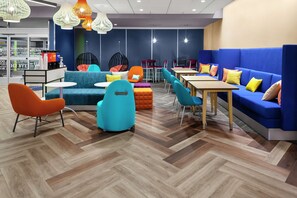 Un área de lounge moderna con suelo de madera en patrón de espiga, asientos en tonos azul y naranja e iluminación colgante.