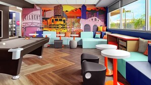Un espacio interior vibrante con mesa de billar, zonas de estar y un mural que representa un paisaje urbano desértico.