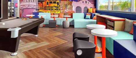 A vibrant indoor space with a pool table, seating areas, and a mural depicting a desert cityscape.