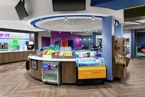A breakfast area with a counter, refrigerated display, and beverage dispensers. - Tru by Hilton Gilbert (Gilbert)