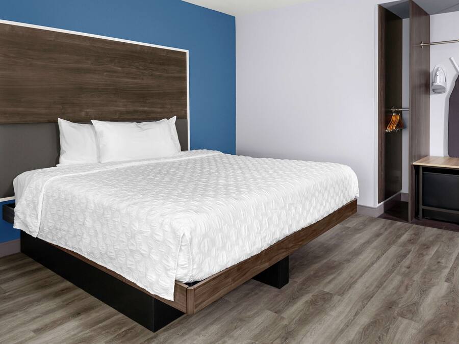 A modern bedroom with a large bed, a wooden headboard, and a built-in wardrobe with a mirror and hanging clothes.