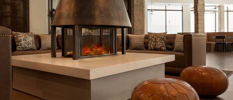 Una sala de estar moderna con chimenea central, otomanas de cuero y un gran ventanal que proporciona luz natural.