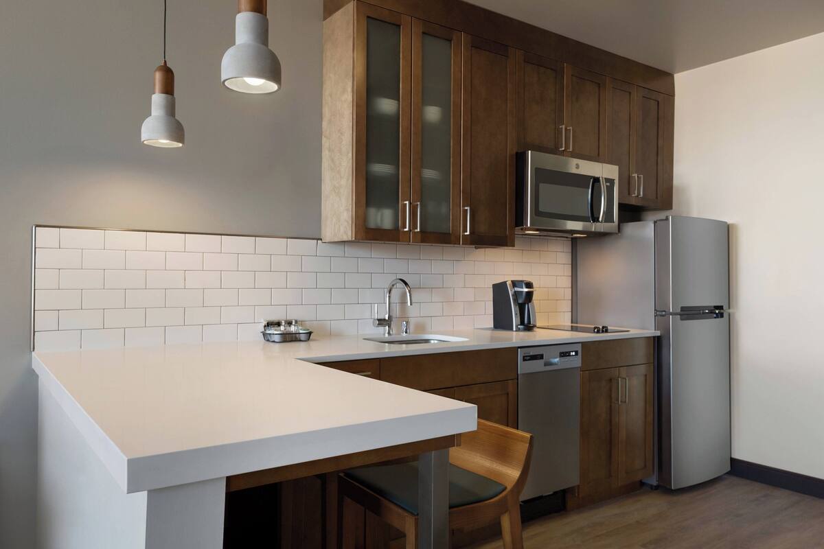A modern kitchen with wooden cabinets, a stainless steel refrigerator, a microwave, and a dishwasher.