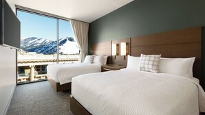 Une chambre d’hôtel avec deux lits, une grande fenêtre donnant sur les montagnes, un téléviseur à écran plat et une tête de lit en bois.