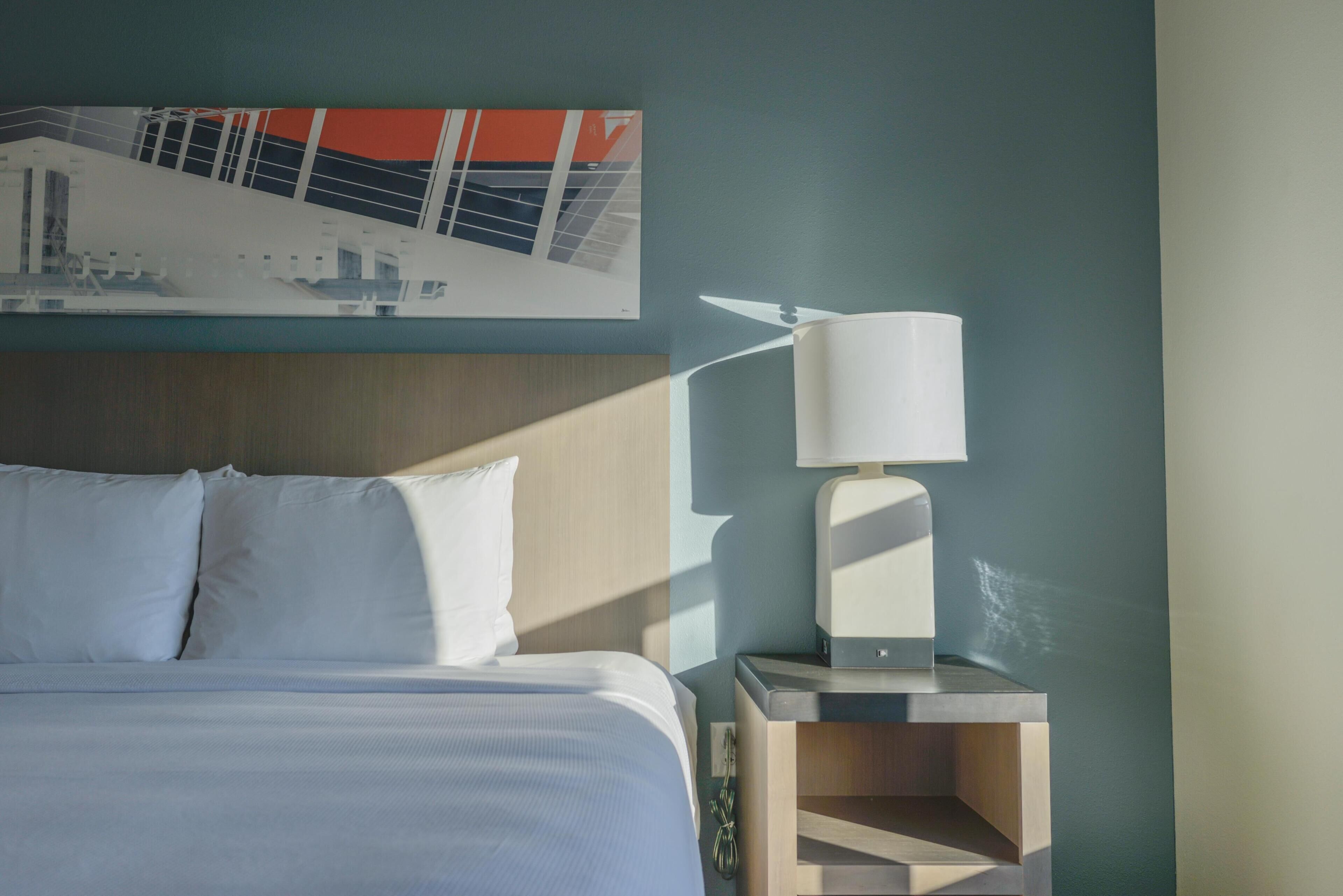 Una habitación de hotel con una cama, una mesita de noche con lámpara y una obra de arte colgada en la pared.