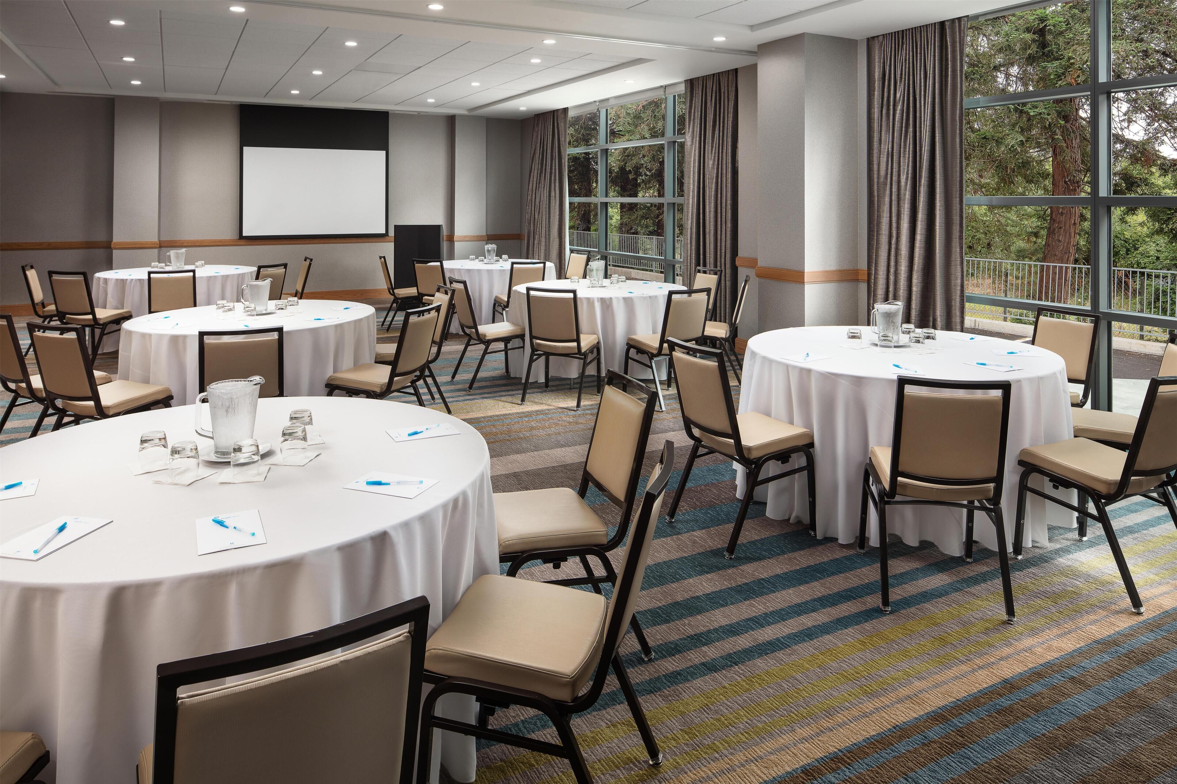 A conference room with round tables, chairs, and a projector screen.