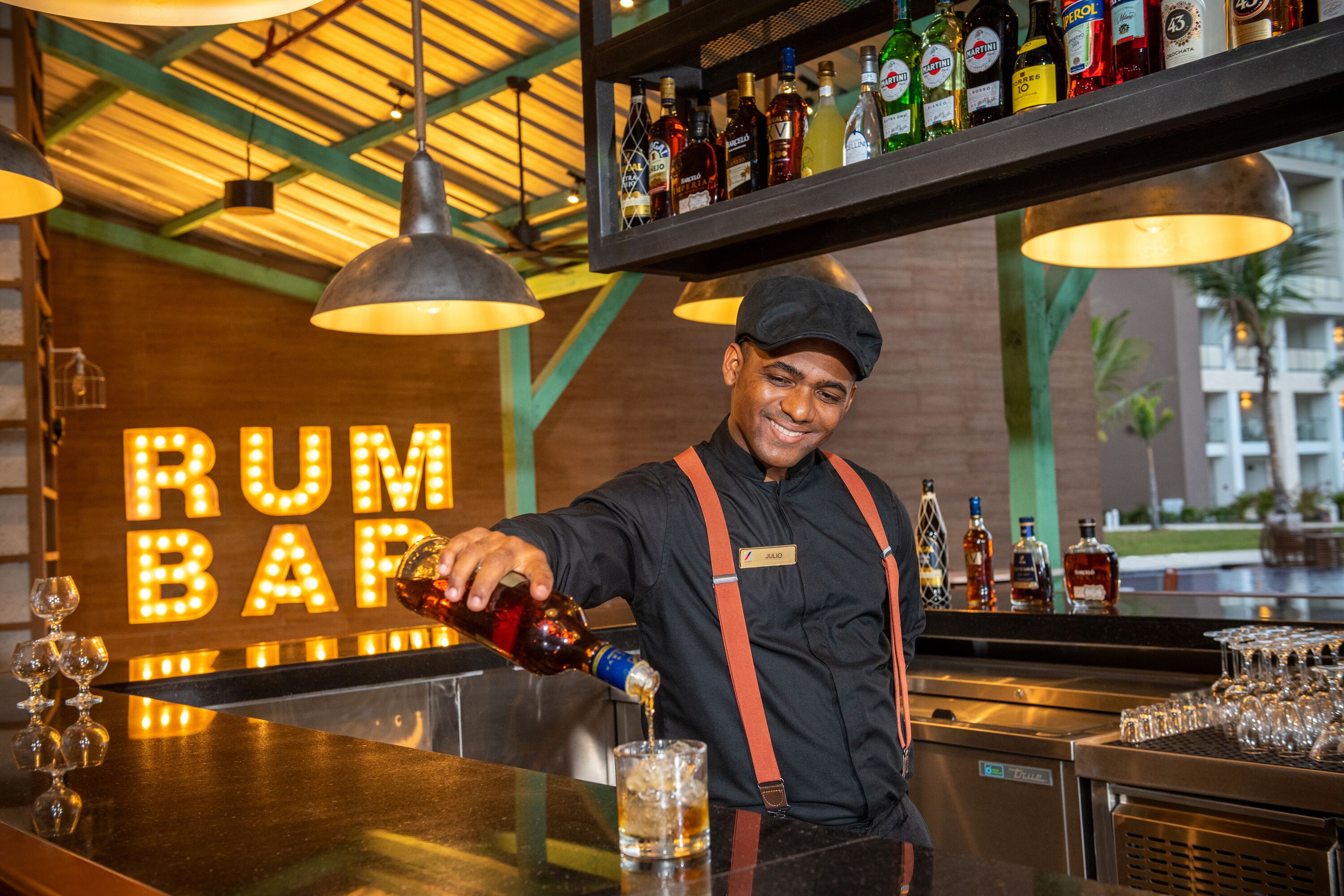 A bartender pouring a drink at a bar with a 'RUM BAR' sign in the background.