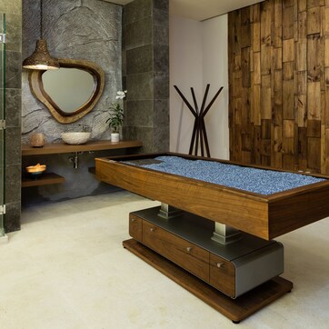 A modern bathroom with a freestanding pool table, a stone wall, and a wooden panel wall.