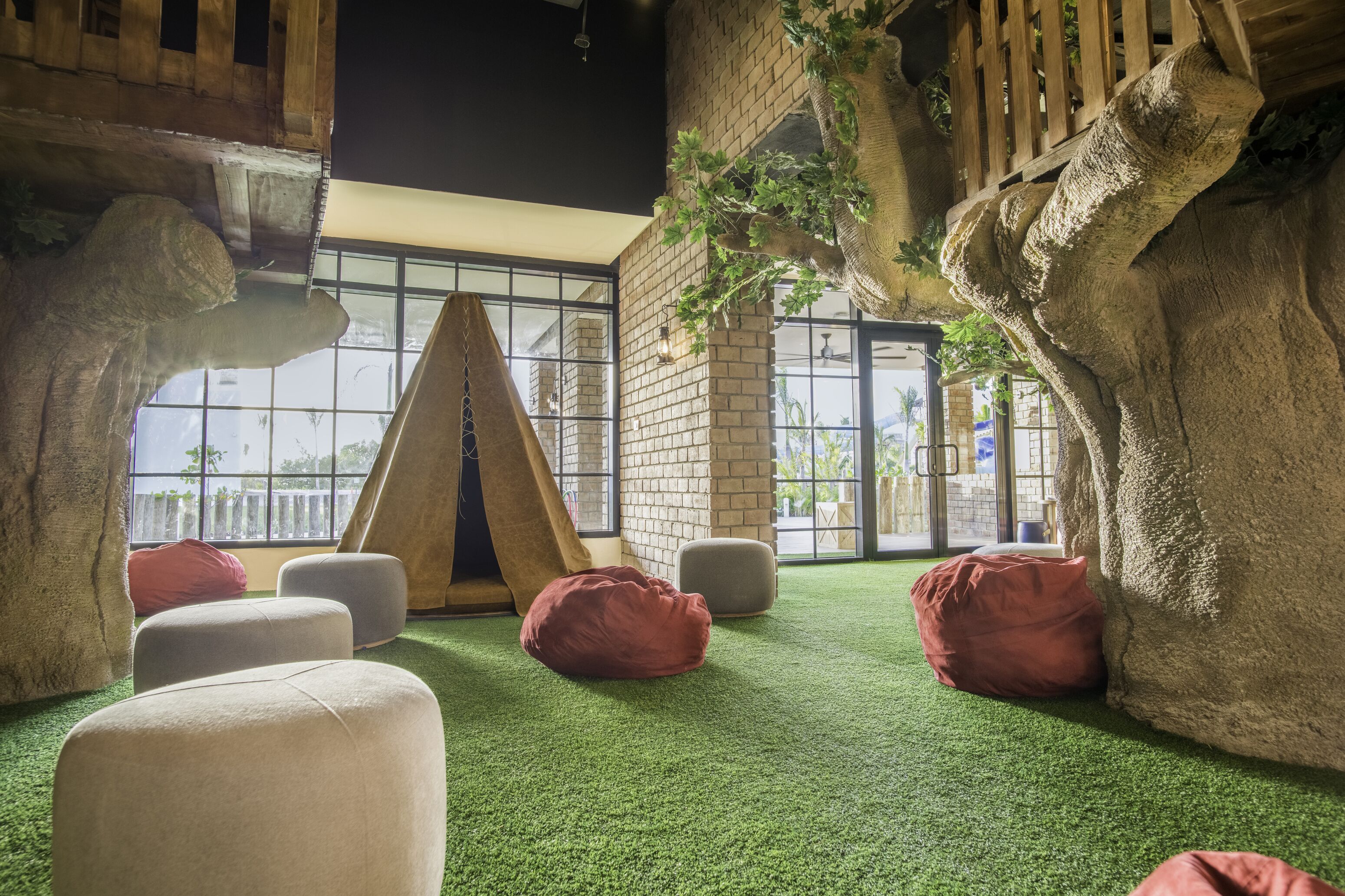 A room with a green artificial turf floor, a large rock wall, and a window with a view of palm trees.