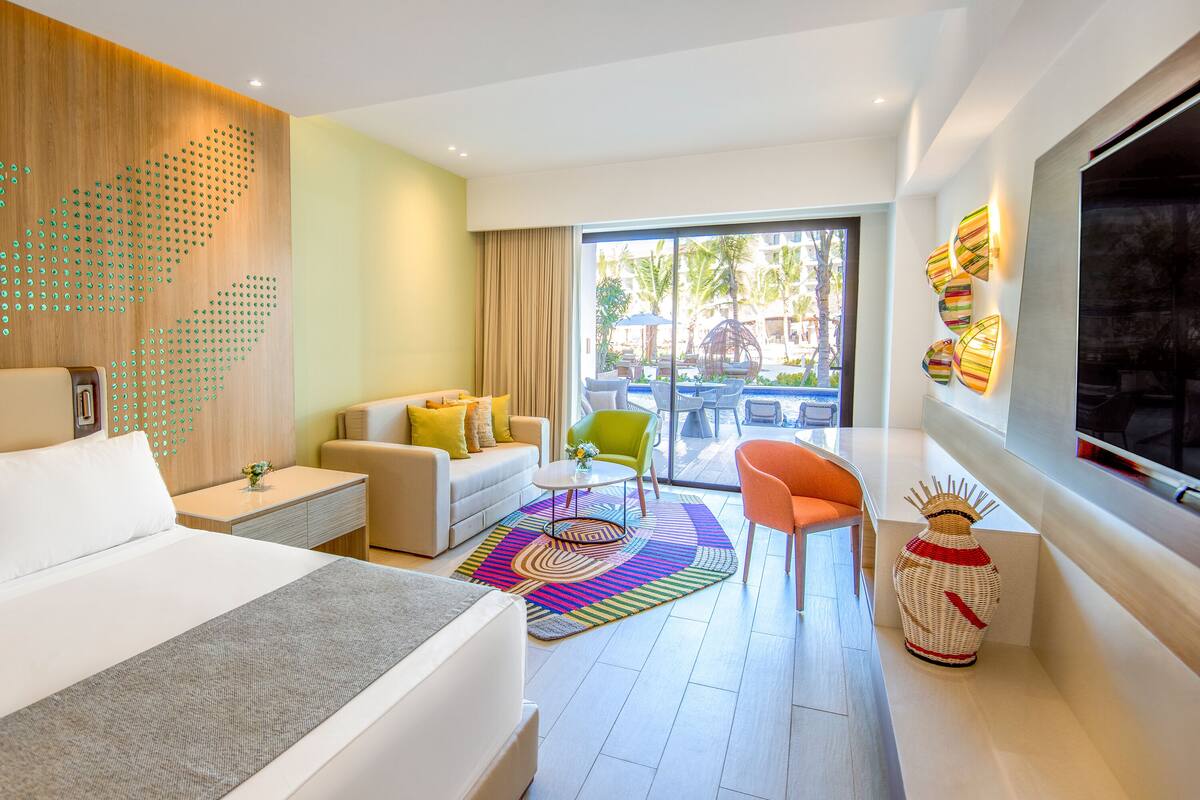 A modern hotel room with a bed, a sofa, a chair, a small table, and a decorative vase.