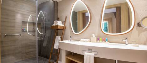 Un baño moderno con cabina de ducha de vidrio, una escalera de madera, un mueble de tocador grande con espejo y un perchero para toallas.