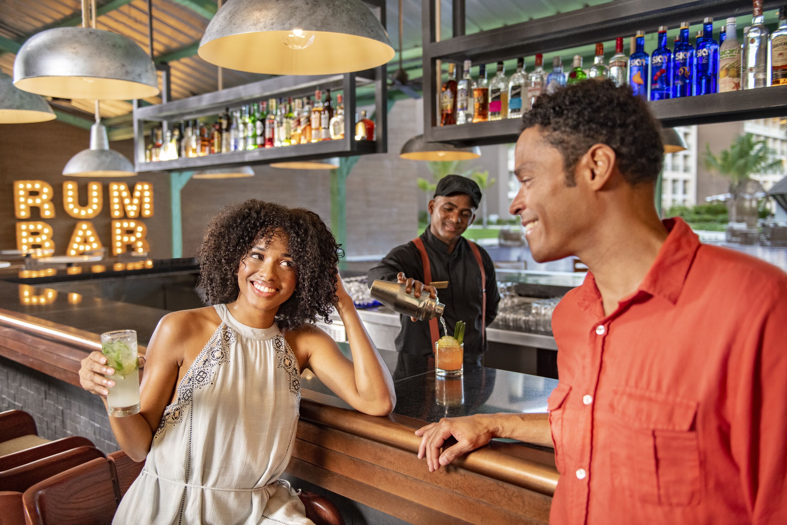 A bar area with a 'RUN BAR' sign, shelves of liquor bottles, and a bartender preparing a drink.