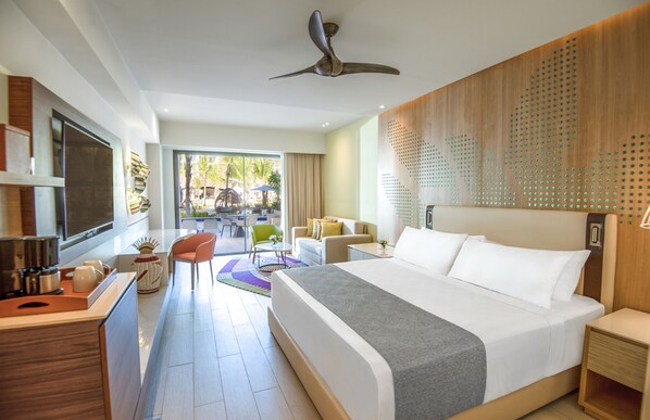 Una habitación de hotel moderna con una cama grande, un escritorio con una silla, un balcón con vistas y un ventilador de techo.