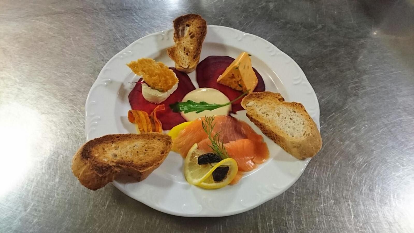 A plate with various food items including bread, smoked salmon, and a beetroot slice.