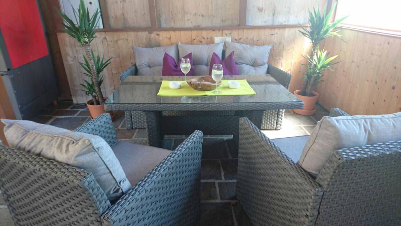 Een terras met rieten meubels, een tafel met een gele placemat en potplanten.