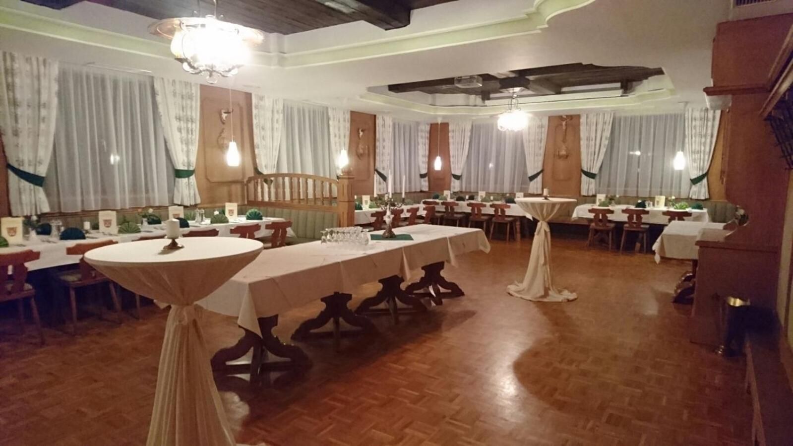 A banquet hall with multiple round tables, wooden flooring, and curtains.