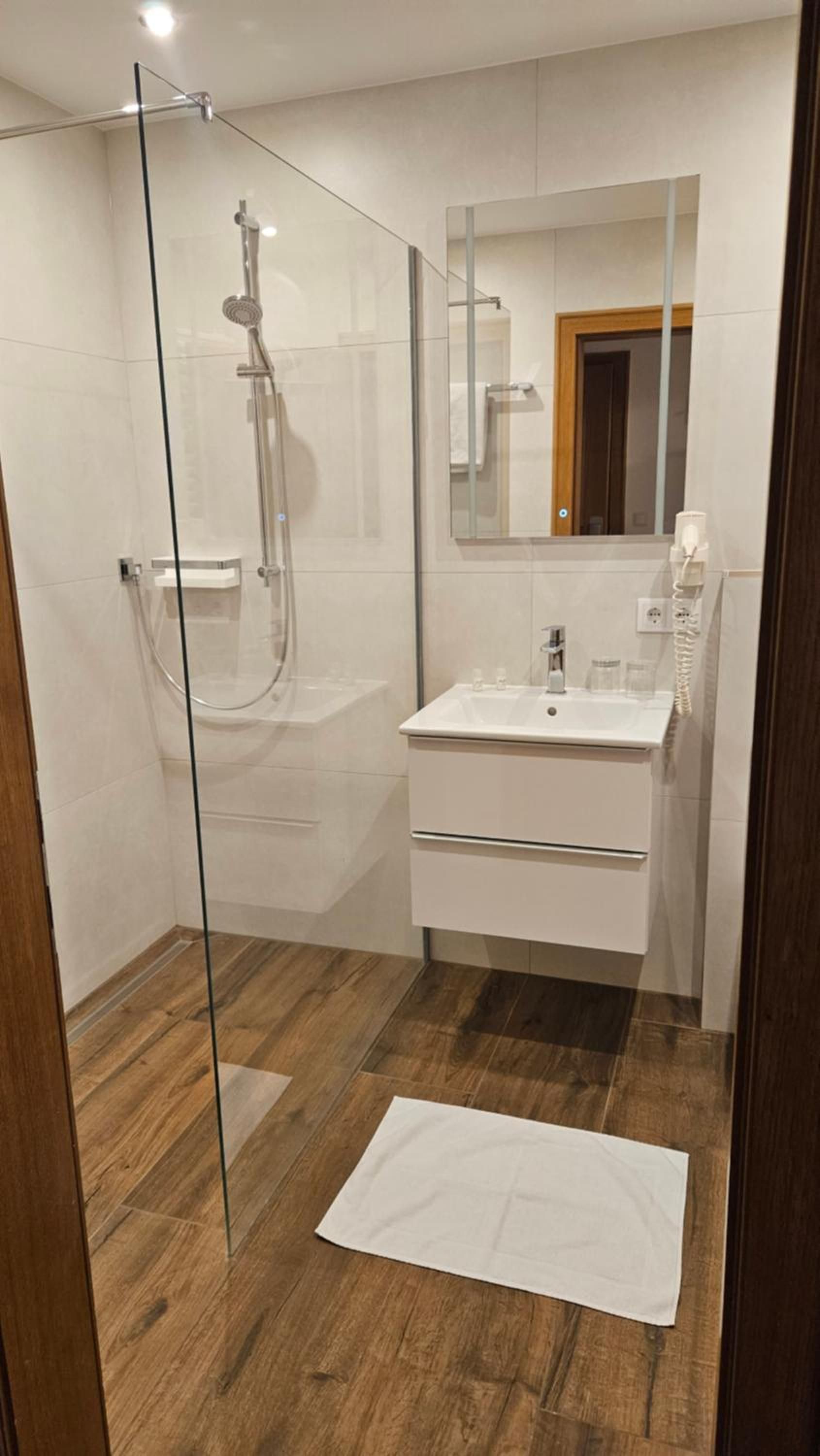 Een moderne badkamer met een douchecabine van glas, een witte wastafel en een spiegel erboven.
