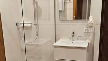 Een moderne badkamer met een douchecabine van glas, een witte wastafel en een spiegel erboven.