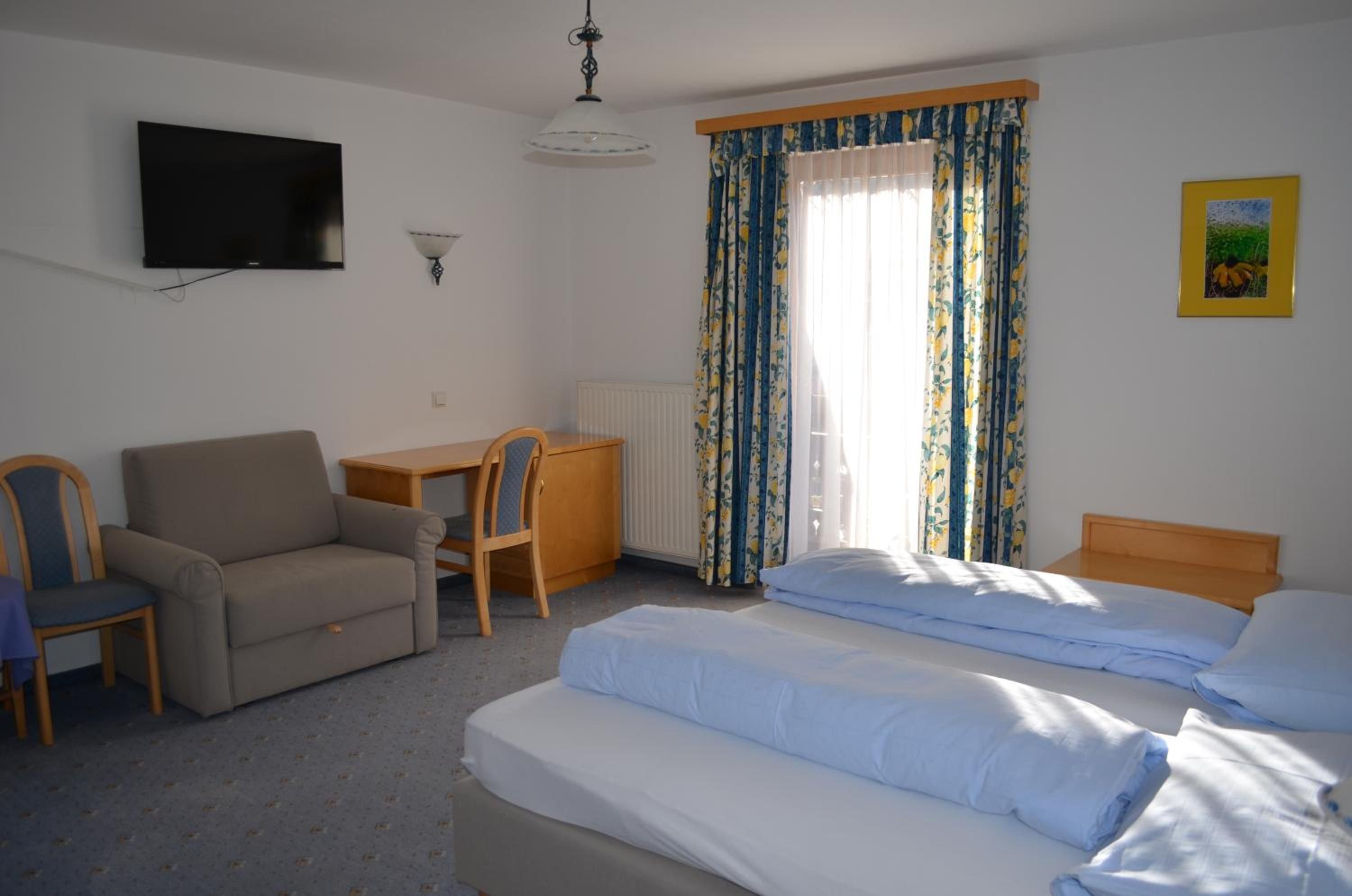 Een hotelkamer met een bed, een bureau, een stoel, een televisie en een raam met gordijnen.