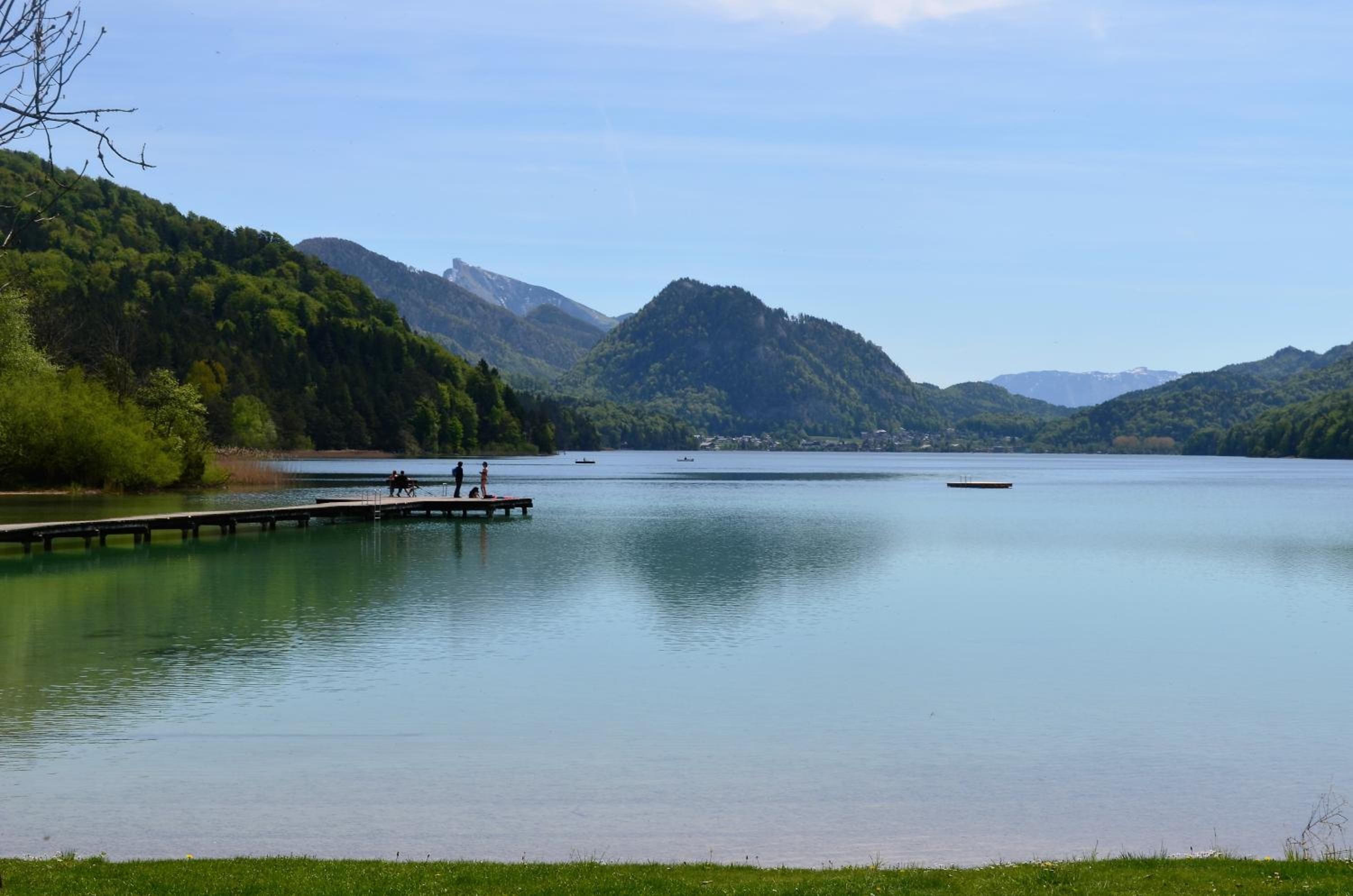 A calm lake with a dock extending into the water, surrounded by forested hills.