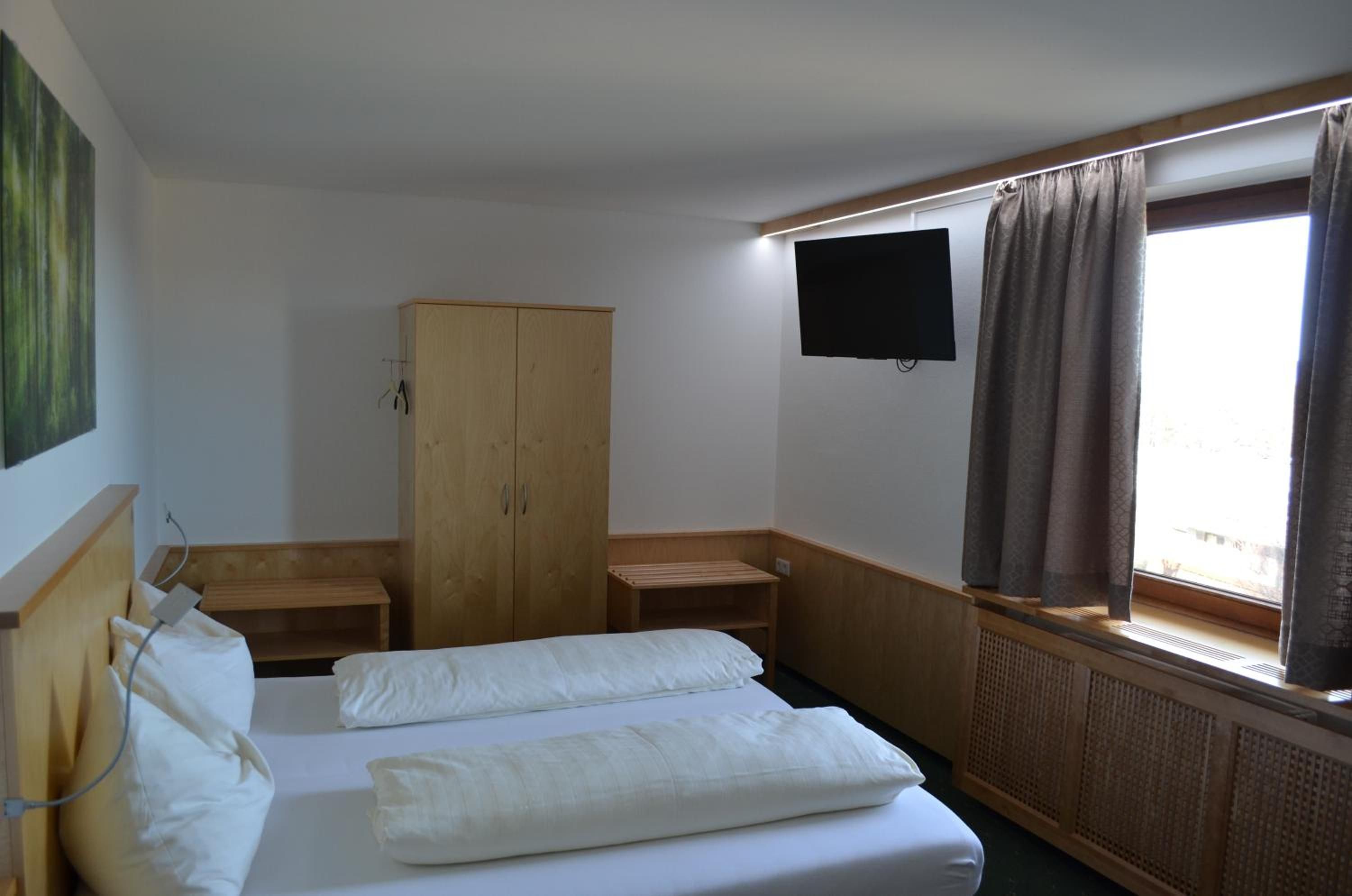A hotel room with a bed, a wooden wardrobe, a television, and a window with curtains.