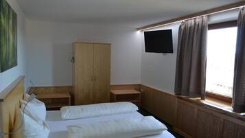 A hotel room with a bed, a wooden wardrobe, a television, and a window with curtains.
