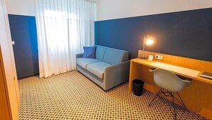 A hotel room with a sofa, a desk, a chair, a lamp, and a patterned floor. - Hotel Otterbach (Bietigheim-Bissingen)