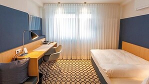 A hotel room with a bed, a desk with a chair, a mirror, and a patterned floor. - Hotel Otterbach (Bietigheim-Bissingen)