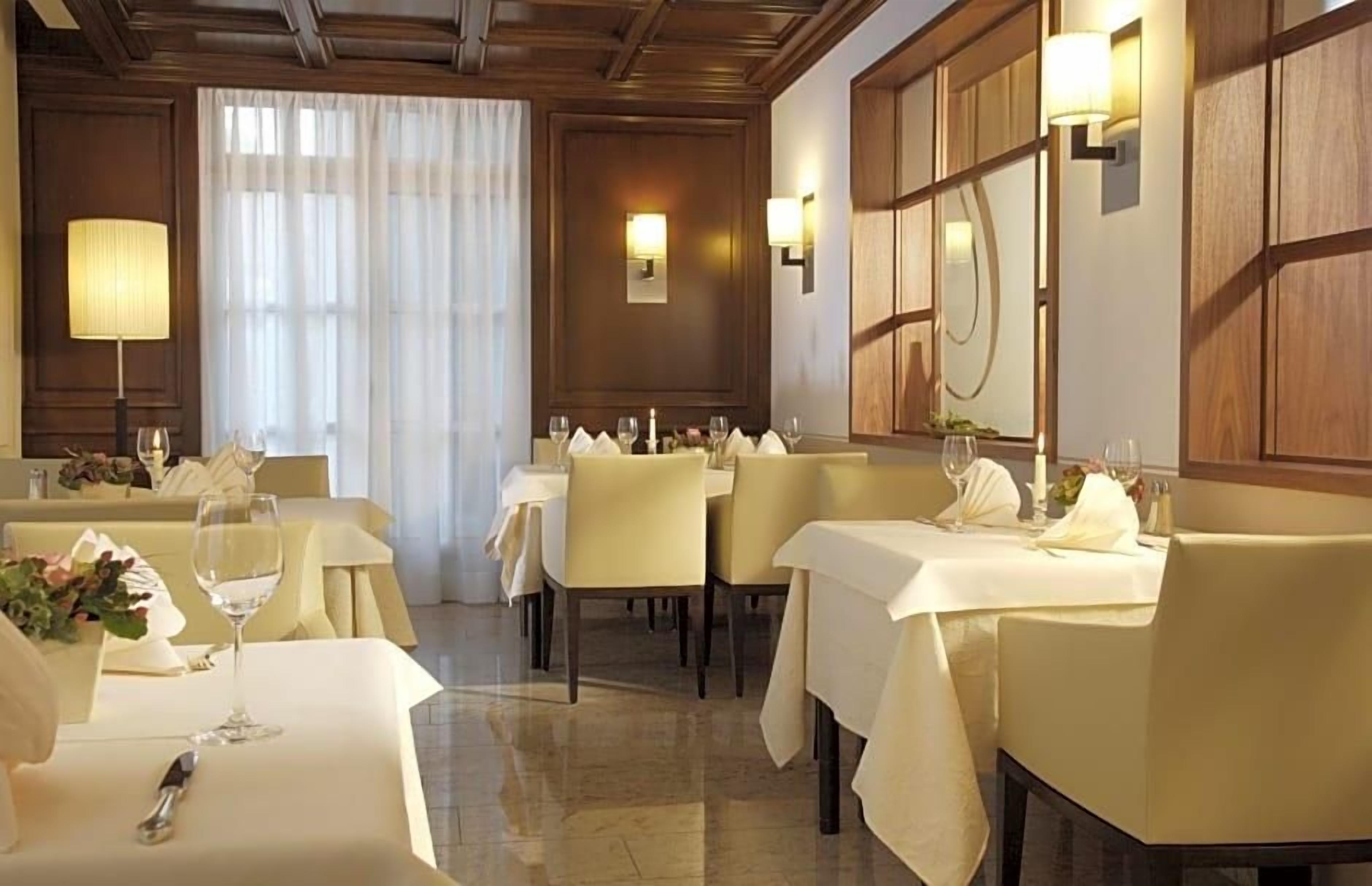 Ein Restaurant mit gedeckten Tischen, einem Chandelier und einem großen Fenster mit Vorhängen.