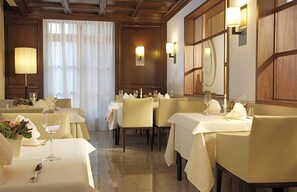 Een restaurant met gedekte tafels, een kroonluchter en een groot raam met gordijnen.