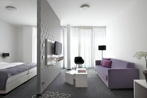 Een moderne hotelkamer met een bed, een bank, een televisie, een kleine tafel en een stoel.