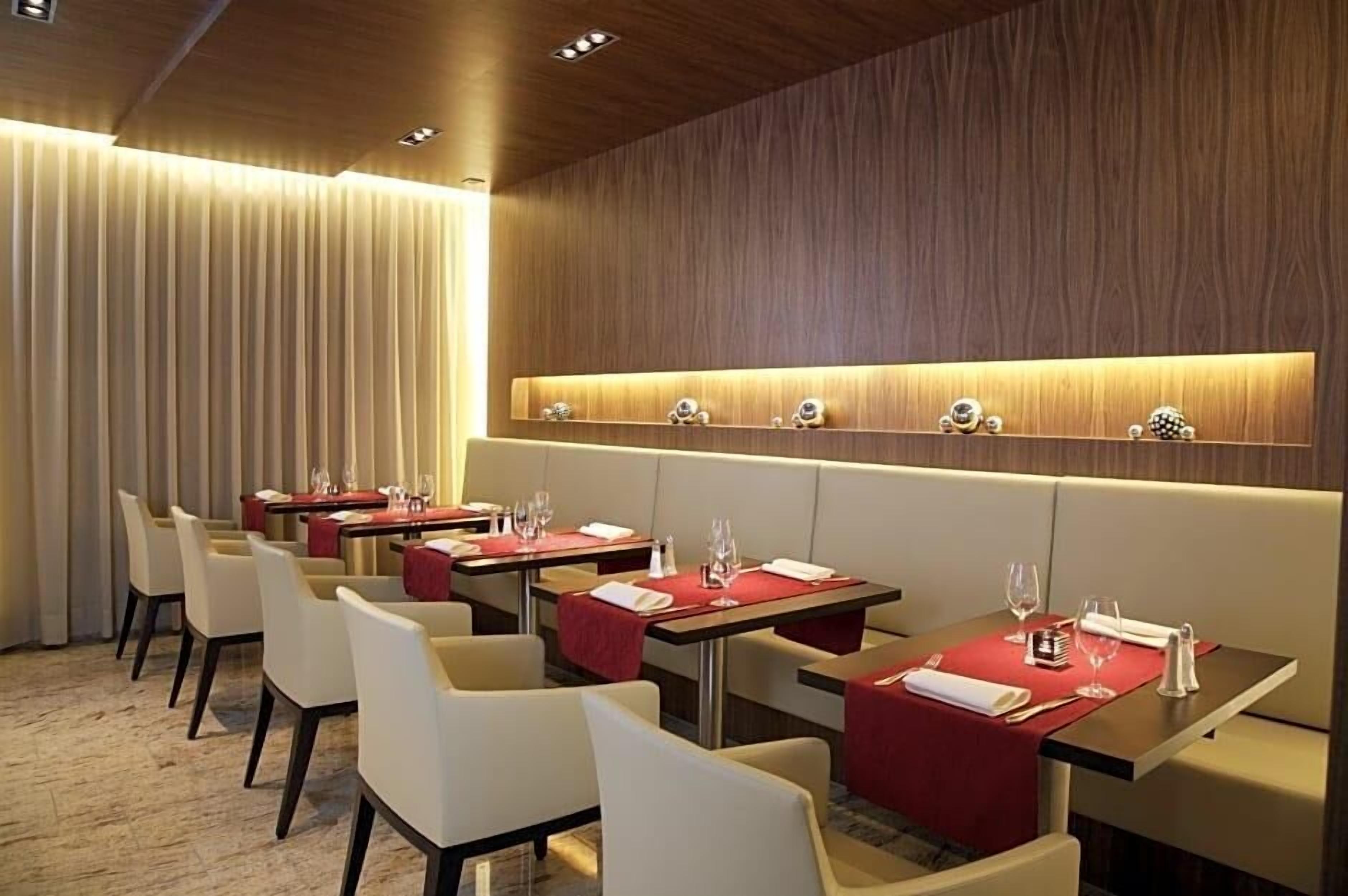 Ein Hotel-Speisesaal mit gedeckten Tischen, einer Holzwand mit beleuchteter Ablage und einem Vorhang im Hintergrund.
