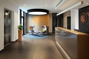 Een moderne receptiebalie met een houten toonbank, twee moderne fauteuils, een grote ronde lamp en een potplant.