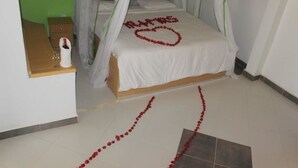 A room with a bed under a canopy, a bedside table with a bottle and glass, and a small wooden cabinet. - Osim Country Lodge (Ewaso Ngiro)