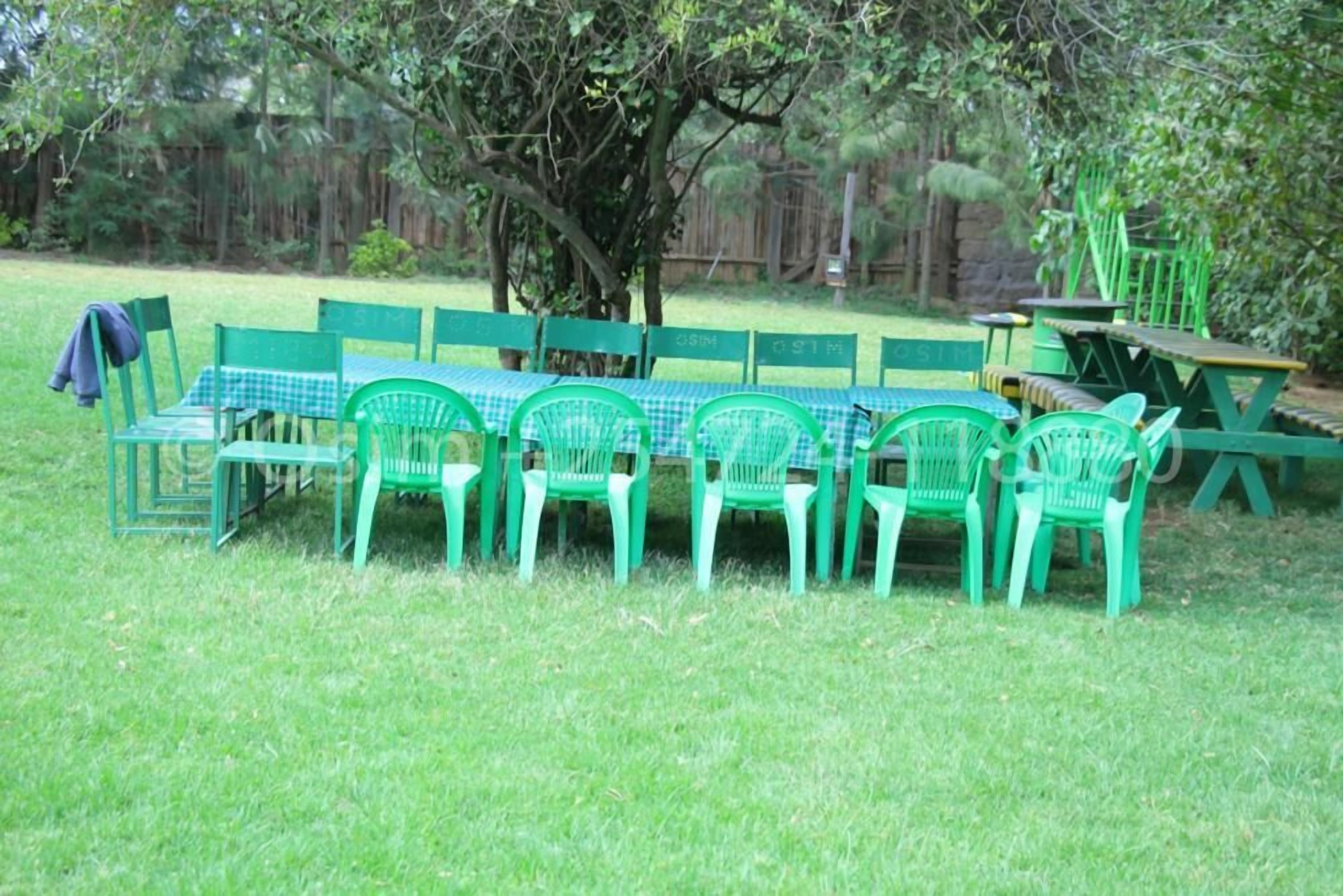 A picnic setup with green plastic chairs and tables arranged on a grassy lawn.
