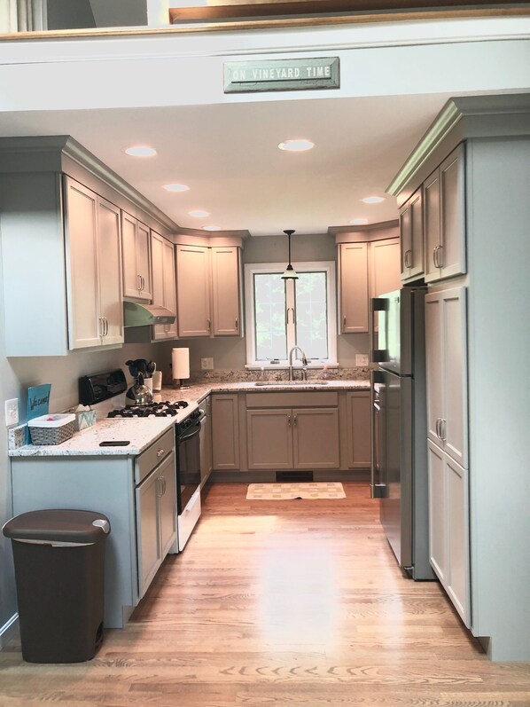 A kitchen with light wood cabinets, a central island, stainless steel appliances, and a window with a view.