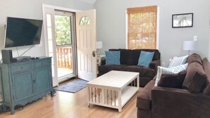 A living room with a television, two couches, a coffee table, and a door leading outside.