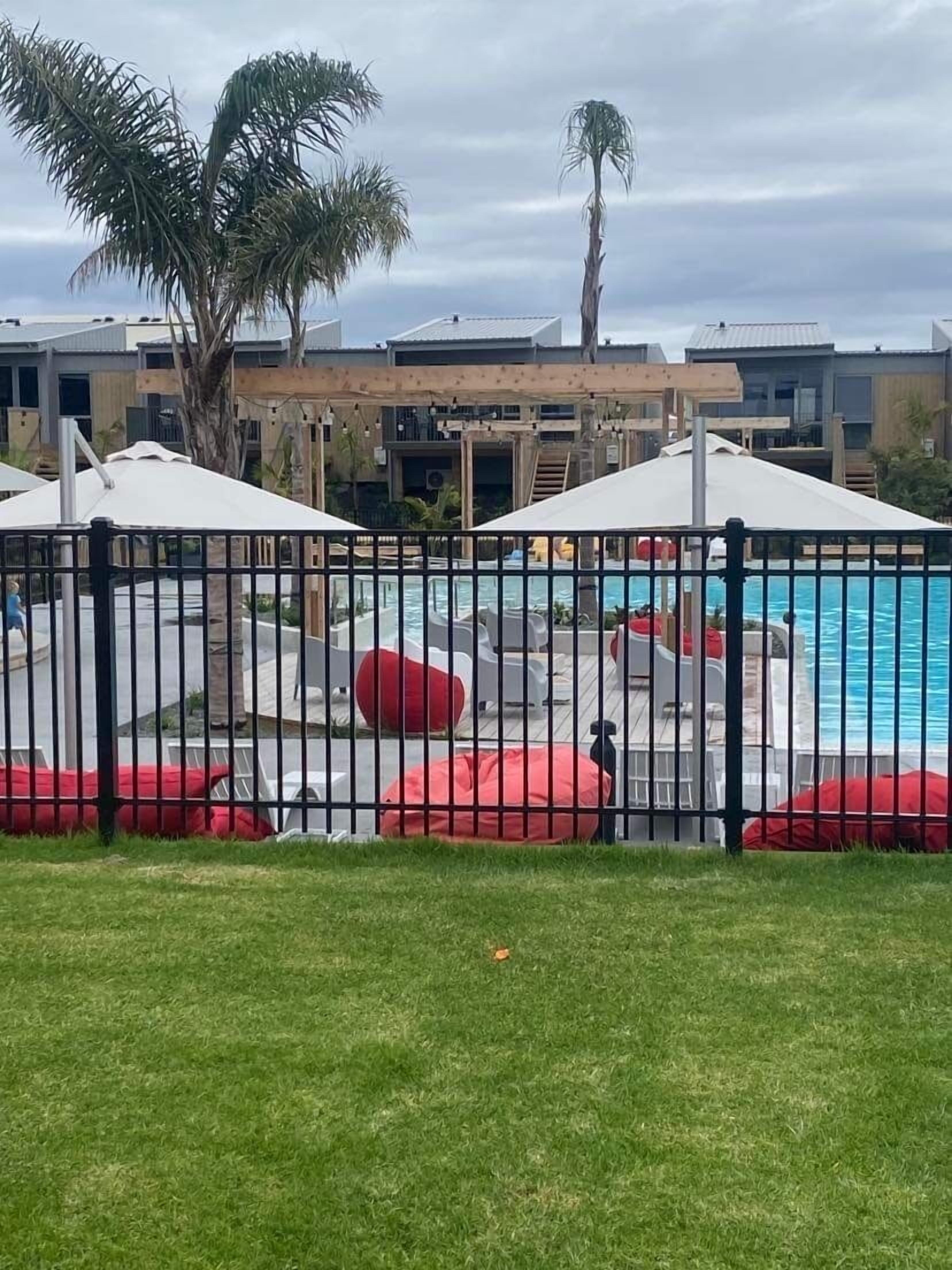 A swimming pool area with a fence, red bean bags, and umbrellas.