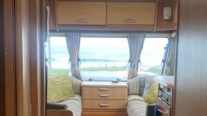 Un intérieur de camping-car compact comprenant un coin cuisine, un lit avec des rideaux et une vue sur l’extérieur.